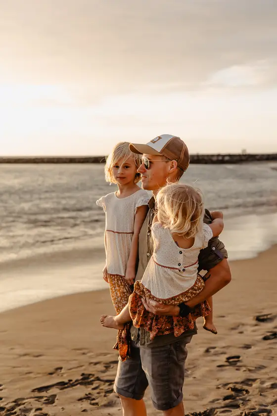 Father carrying two daughters in arms during beach lifestyle family session